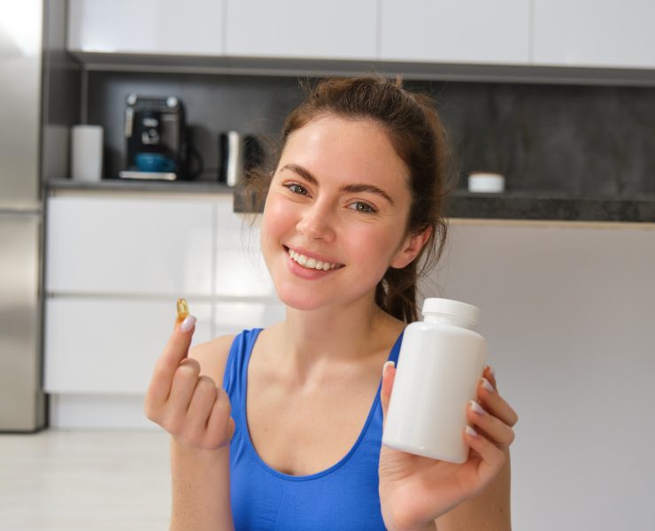 Happy young fit girl, doing sports at home, shows dietary supplements, taking vitamins for healthy body, recommending, showing drug capsule